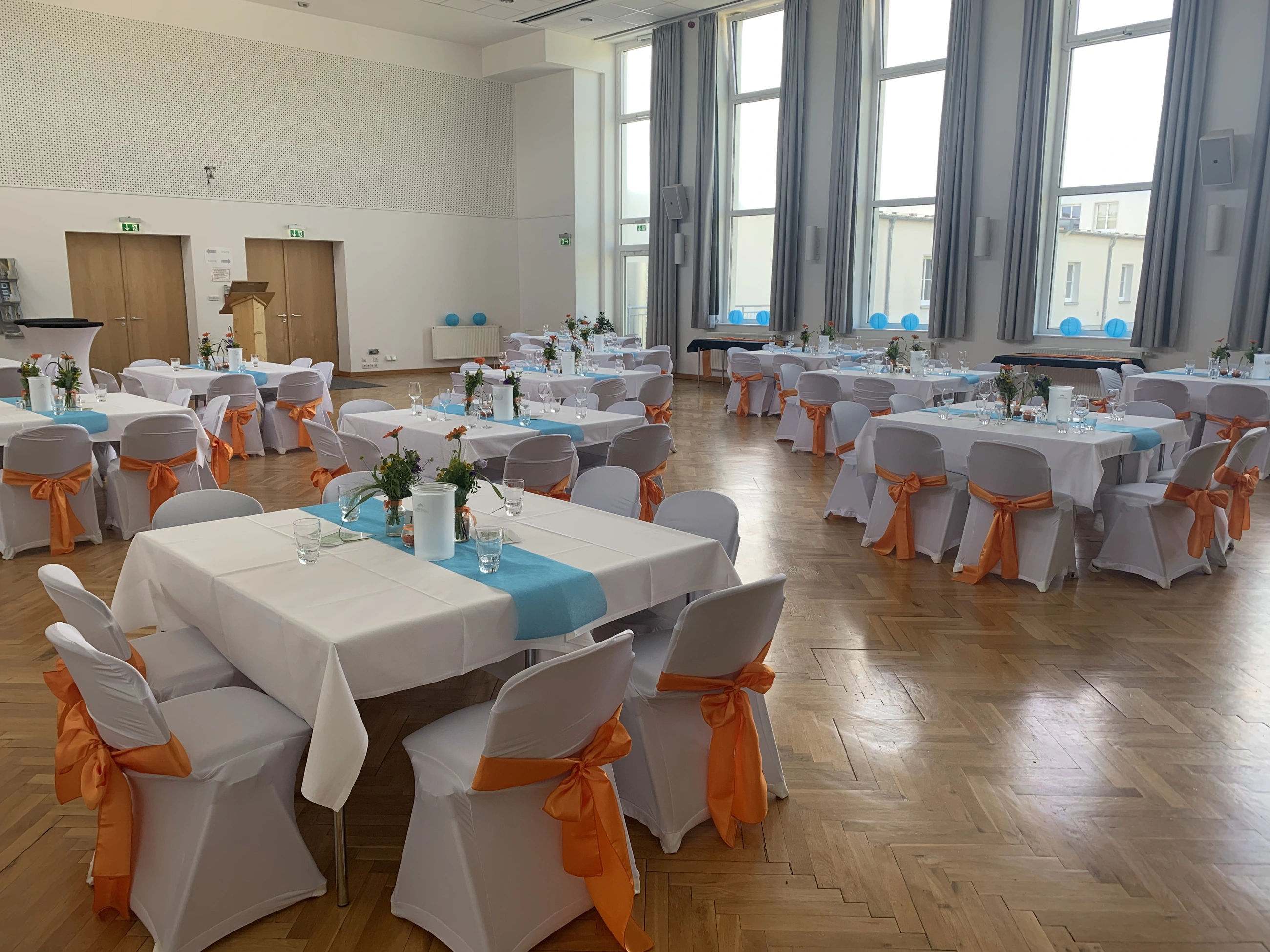 Hochzeitsdekoration im großen Saal mit türkisen Tischläufern und orangefarbenen Schleifen