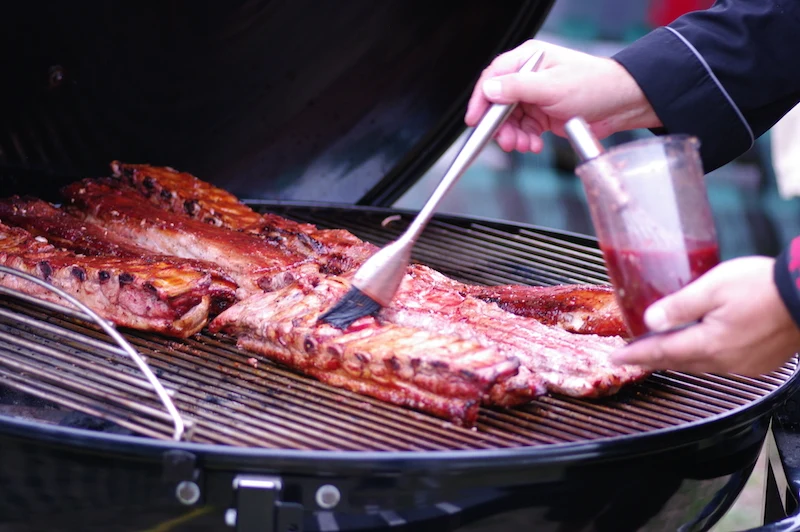 Rippchen werden mit einer Grillzange auf dem Rost gewendet